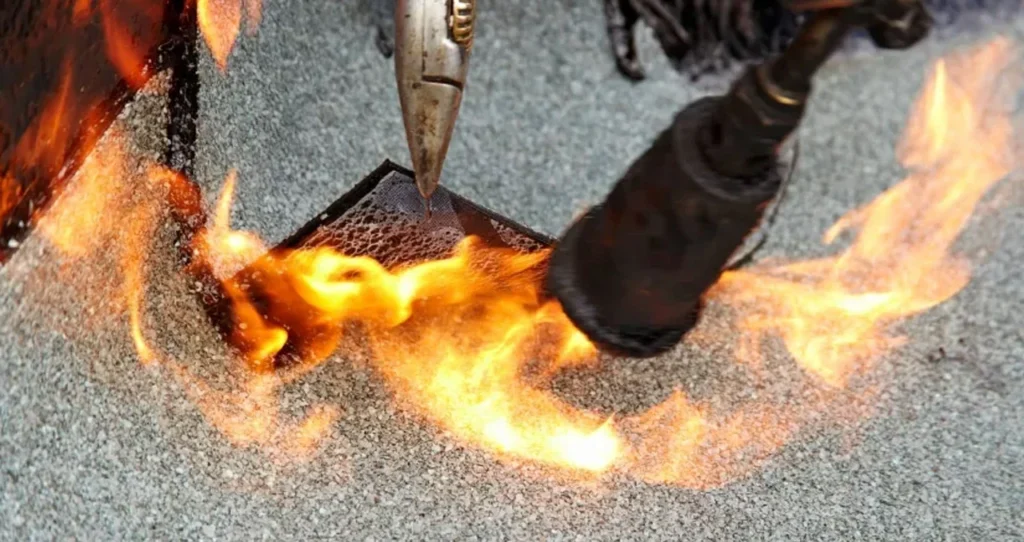 Dakdekker brandt een bitumen reparatiestuk vast op een plat dak in Houten