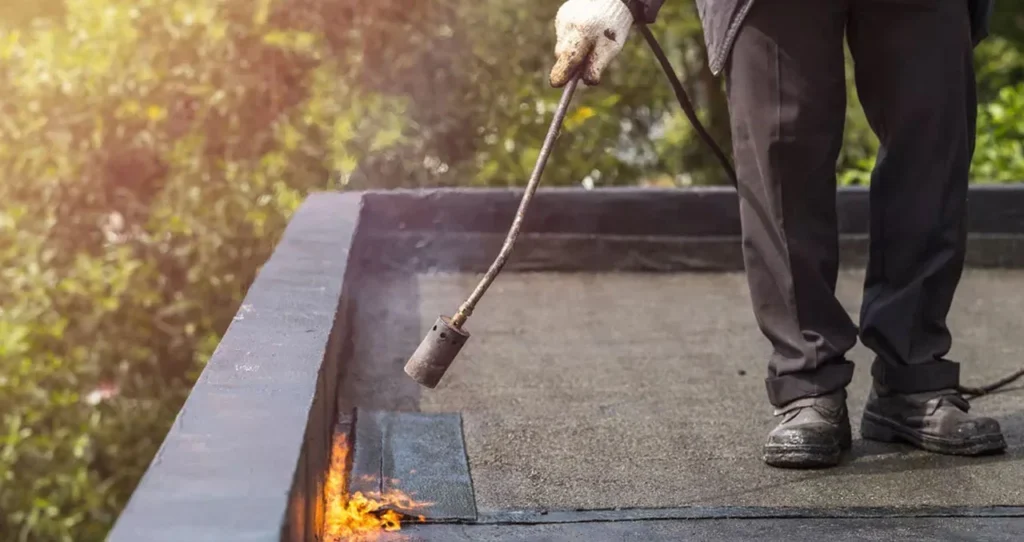 Dakdekker brandt bitumen dakbedekking af langs de dakrand van een plat dak in Nieuwegein