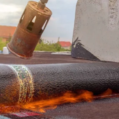 Brander verwarmt een rol bitumen dakbedekking op een plat dak in Ijsselstein
